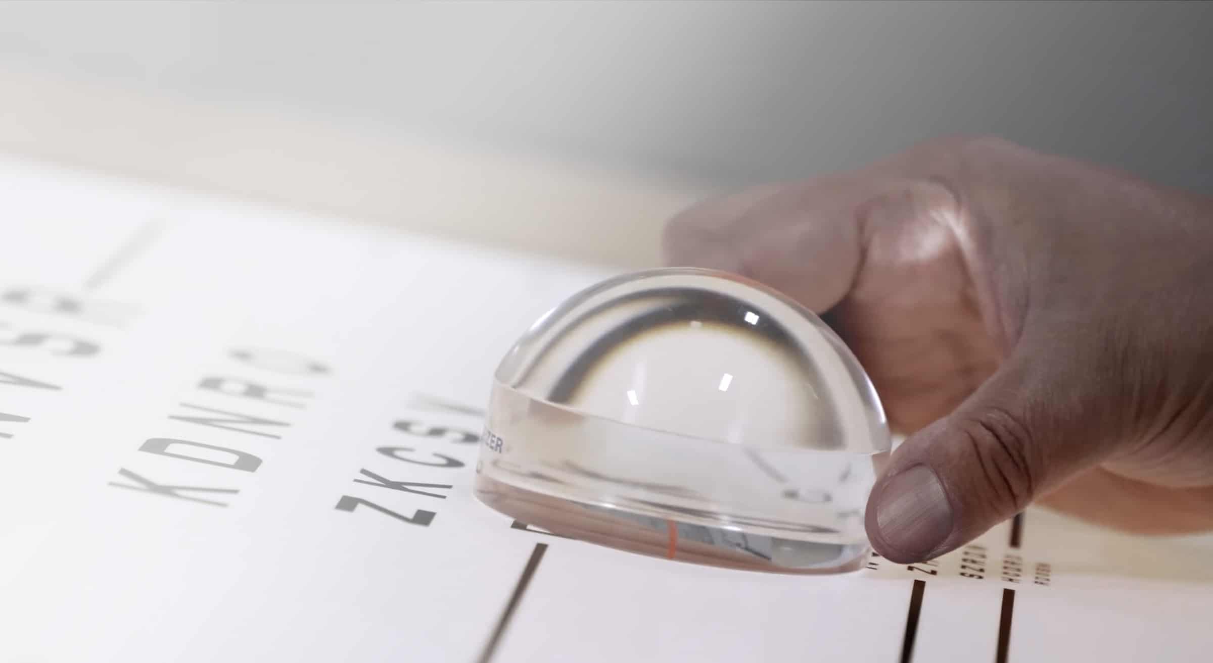 Hand holding a clinical vision lens over a Sloan letter eye chart — Precision Vision homepage hero