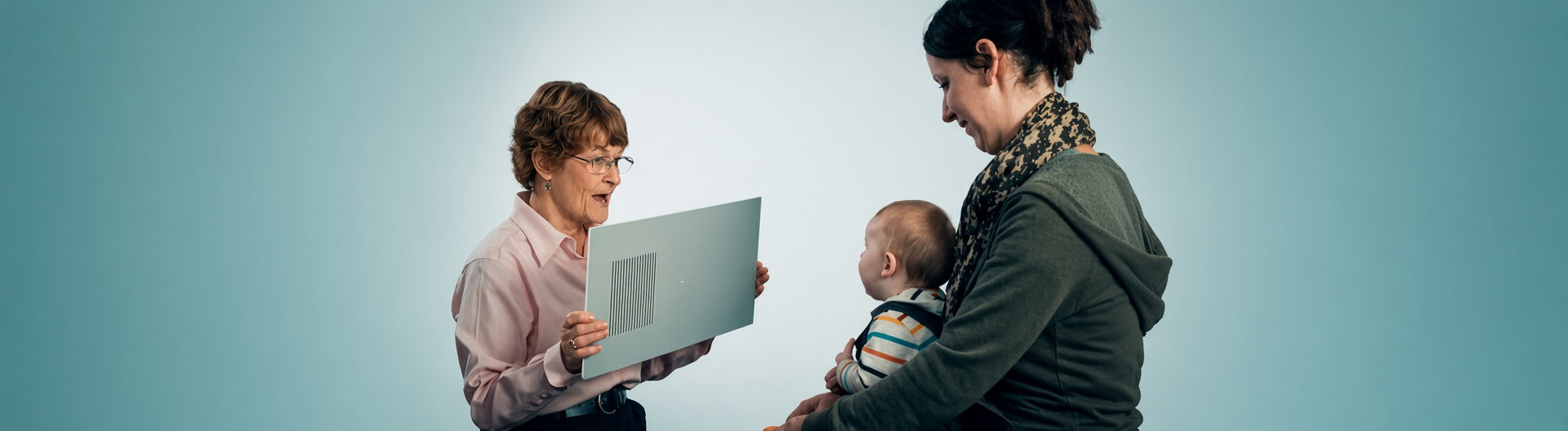 A clinician holds a Teller Acuity Card up to an infant seated on a parent's lap, presenting the striped grating during a preferential looking vision test